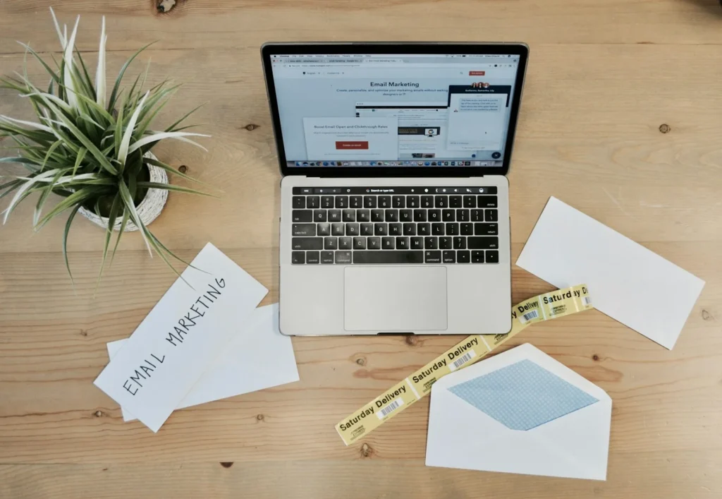 Open laptop on a wooden desk beside printed pages and a plant