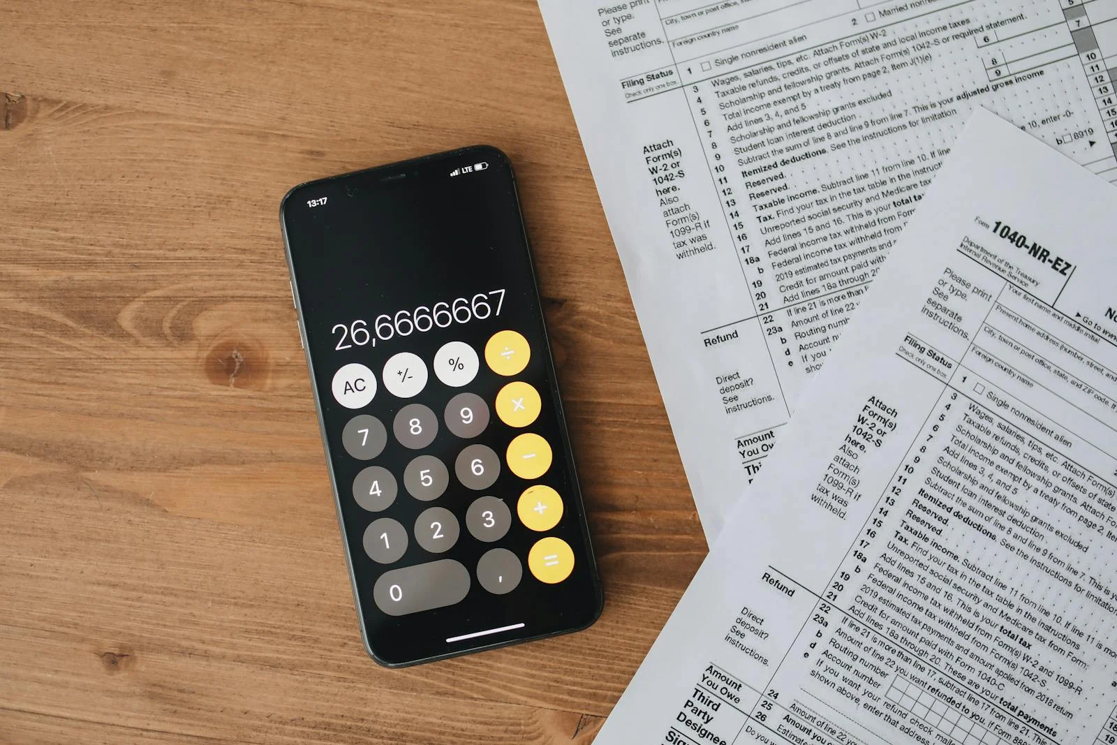 Smartphone calculator next to tax forms on a wooden desk